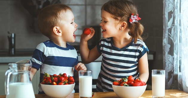 Niña y niño comiendo fresas de un plato hondo